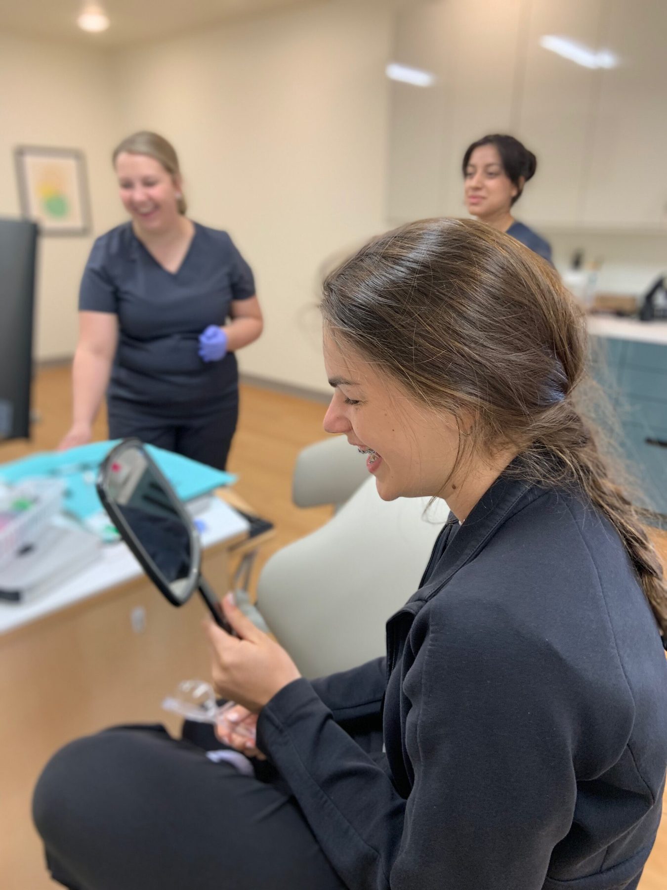 A patient sees her new braces in a hand mirror as two Hodge staff look on.