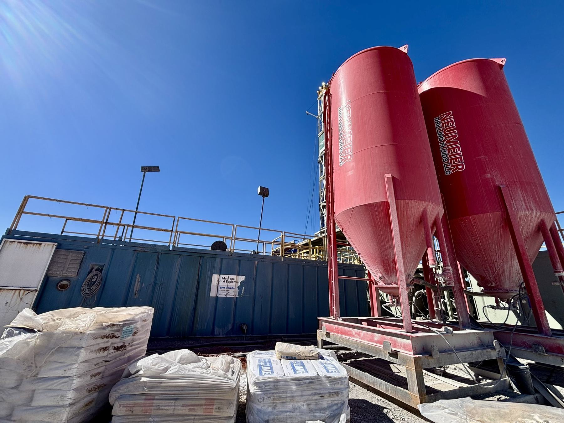 Bulk-material silos on a rig site with pallets of sacked product.