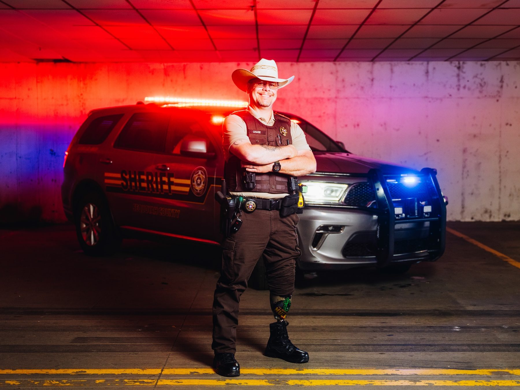 A sheriff’s deputy with a patterned prosthetic lower leg in front of his patrol vehicle.