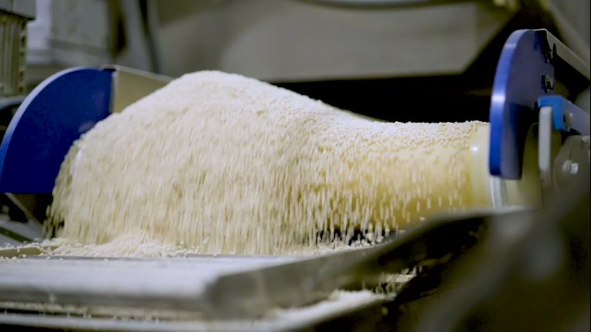 Extruded crisps cascading over a conveyor end-roller into a collection pan.