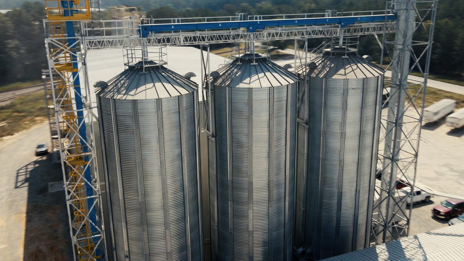 Grain storage bins, overhead conveyor gallery, rail siding and a waiting trailer.